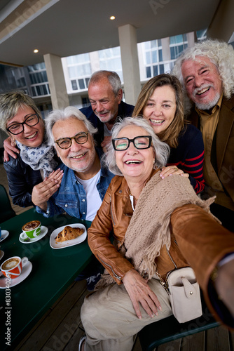 Vertical. Happy mature gray hair woman taking selfie of group seniors Caucasian cheerful friends posing together sitting at cafeteria. Older people looking laughing at camera with snacks on table