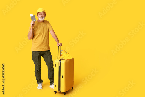 Mature man with passport and suitcase on yellow background. Travel concept