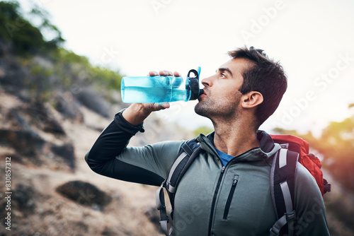 Hiking, fitness and man drinking water in nature with backpack for workout, training and adventure. Sports, liquid or thirsty athlete with refreshing drink in forest for trekking, challenge or travel