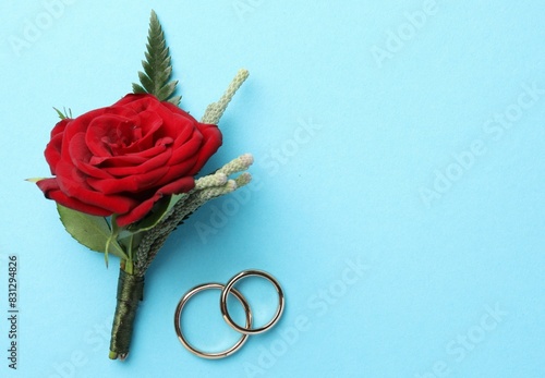 Small stylish boutonniere and rings on light blue background, top view. Space for text