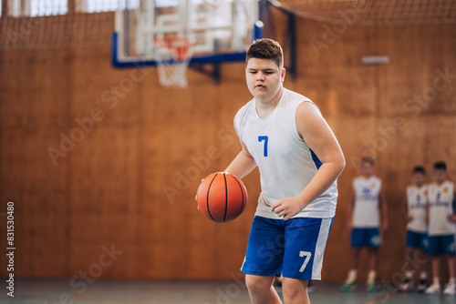 A young basketball kid dribbling a ball on training at indoor court.
