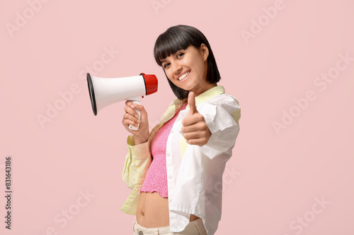 Young woman with megaphone showing thumb-up on pink background
