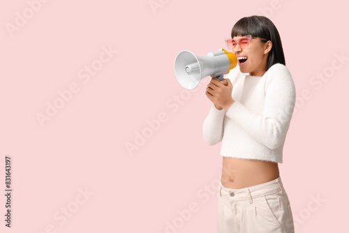 Screaming young woman with megaphone on pink background