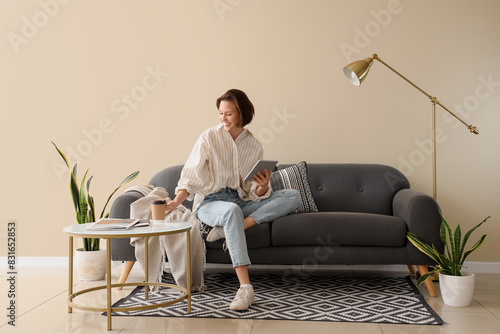 Young pretty woman using tablet and drinking coffee on sofa in light living room