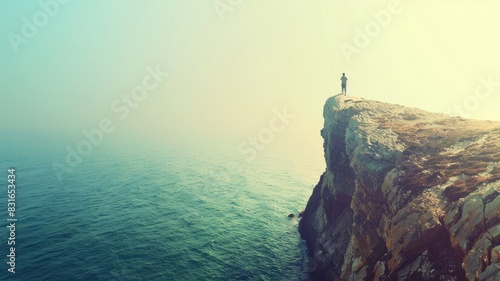 Lone person stands at edge of cliff overlooking vast, misty ocean