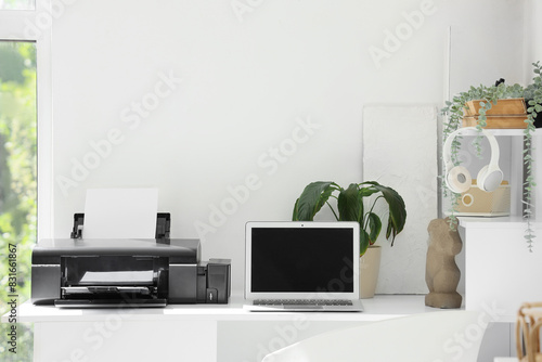 Modern printer and laptop on desk in light office