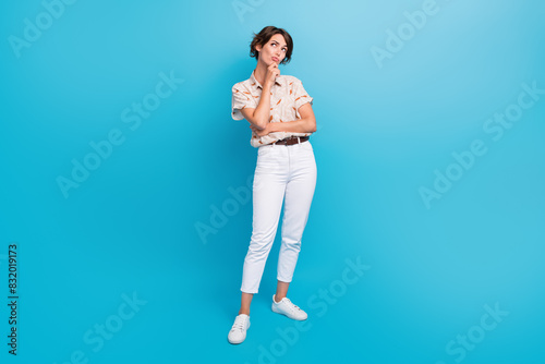 Full size portrait of minded doubtful girl arm touch chin look interested empty space isolated on blue color background