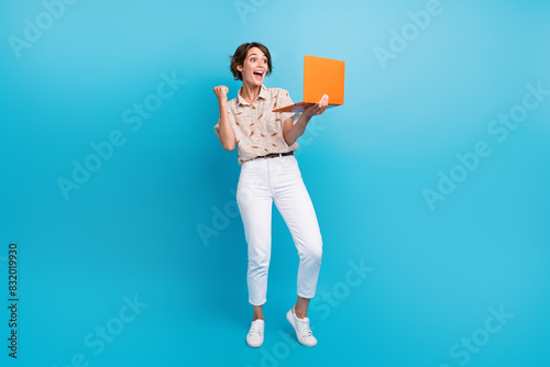 Full size portrait of glad positive girl use laptop raise fist shout yes hooray achievement isolated on blue color background