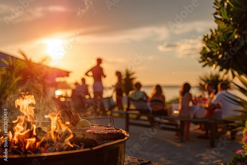 Group of people enjoying a sunset beach barbecue, gathered around a fire and socializing with the ocean in the background.