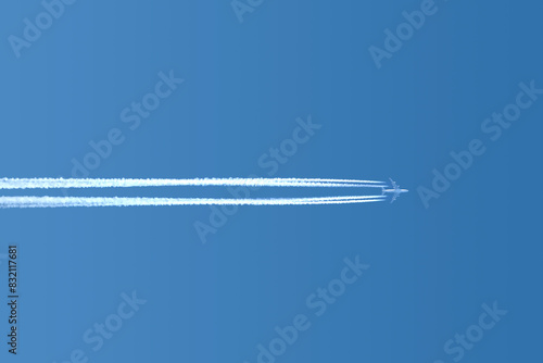 Large four engine passenger supersonic airplane flying horisontal from left to right high in blue cloudless sky leaving long white tracks