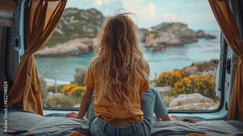 A blond woman in a yellow top looks out from a camper van at a stunning coastal line with cliffs and blue sky