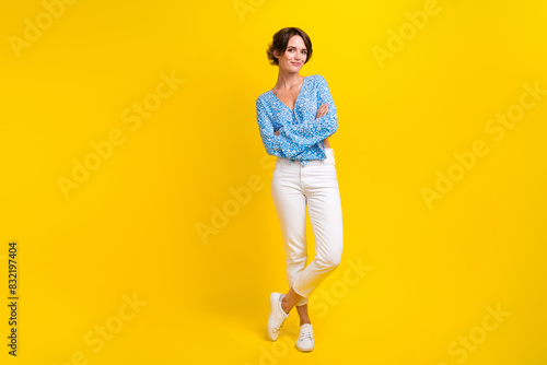 Full length photo of cool optimistic woman dressed print blouse white trousers standing arms crossed isolated on yellow color background