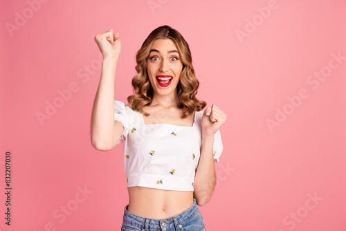 Photo portrait of pretty young girl raise fists winning wear trendy white outfit hairdo isolated on pink color background