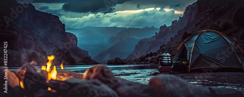 Scenic campsite by a river with a tent, campfire, and colorful sunset in a picturesque canyon landscape.