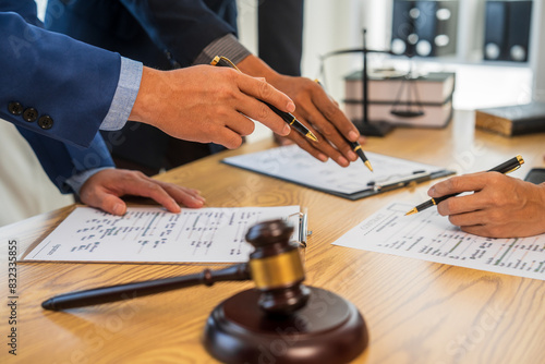 A team meeting of business people and a lawyer in formal suits is taking place at a desk, discussing a contract and various aspects of the law and litigation.