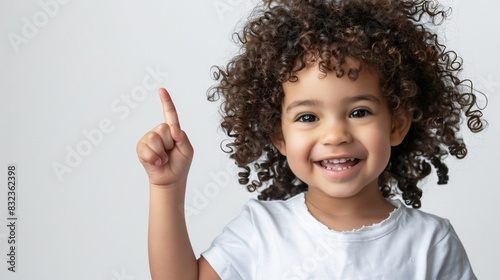 Portrait of a little girl with curly hair, smiling and pointing to up, on a light background