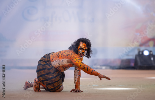 Portrait of an male artist performing classical dance kuchipudi as tiger to save himself from hunter on stage with tiger makeup on his face and body.