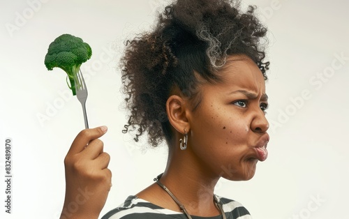 Mujer afroamericana con brócoli en un tenedor, con expresión de disgusto, aislada sobre fondo blanco.