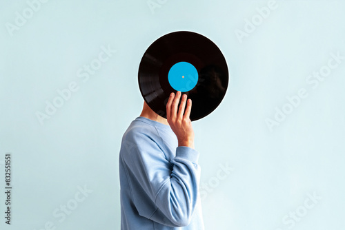 Man in blue sweatshirt covers his face with vinyl record on blue background