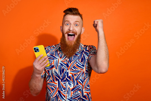 Photo of lucky excited guy dressed print shirt winking winning game modern device empty space isolated orange color background
