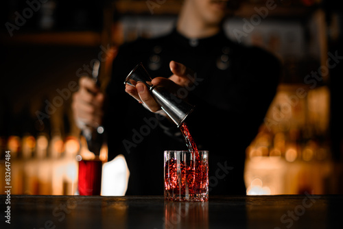 Bartender pours alcoholic beverage for cocktail from jigger into low glass