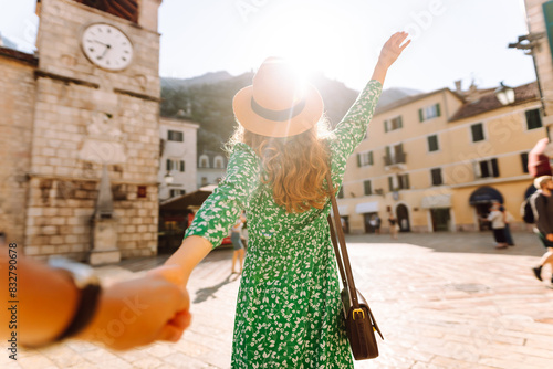 Follow me concept and traveling together. Girl traveler wearing dress, holds the boyfriend's hand and walking on street city. Vacation, tourism.