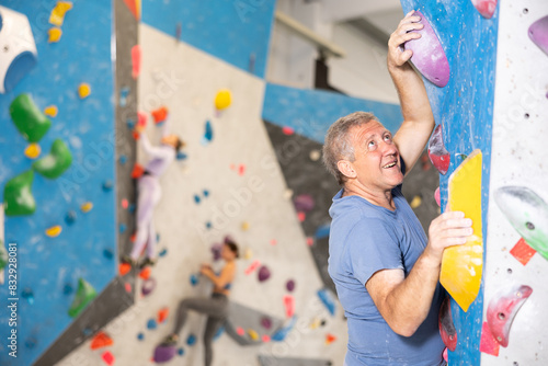 Focused active aged man climbing on bouldering wall demonstrating physical strength, technical skill, and determination.