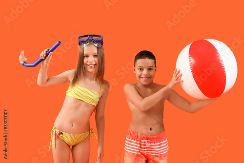 Cute little children in swimsuit with beach ball and snorkeling mask on orange background