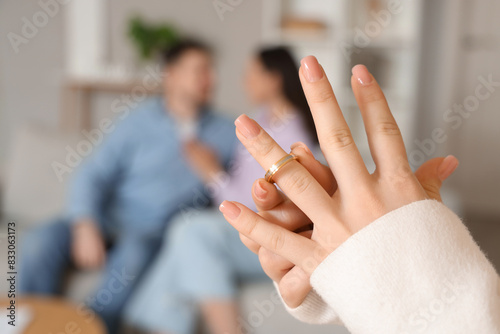 Young woman taking off wedding ring and her husband with mistress at home, closeup. Cheating concept