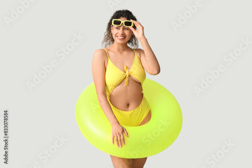 Beautiful young African-American woman in stylish yellow swimsuit with inflatable ring on grey background