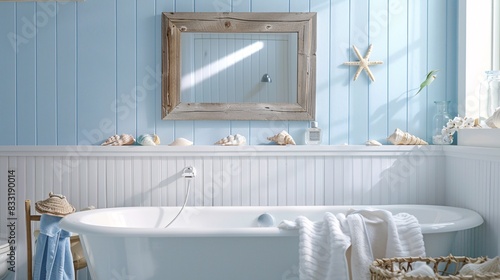 A serene, coastal-inspired bathroom with light blue walls, white wainscoting, and nautical decor. The space features a built-in bathtub, driftwood-framed mirror, and seashell accents, creating a