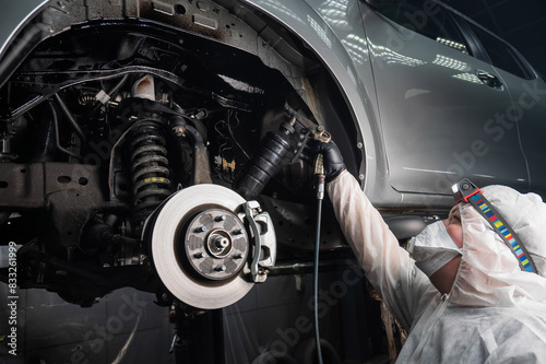 An auto mechanic applies anti-corrosion mastic to the underbody of a car.