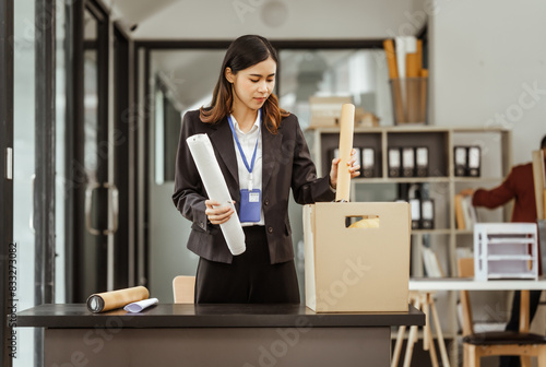 A young Asian businesswoman in a formal suit is working at her desk, preparing to resign after being laid off. She carefully drafts her resignation letter and plans her next steps.