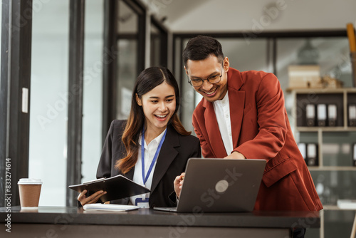 Middle-aged businessman and young Asian businesswoman diligently working at desks, managing tasks as recruitment, training, performance management, inclusive organizational culture.