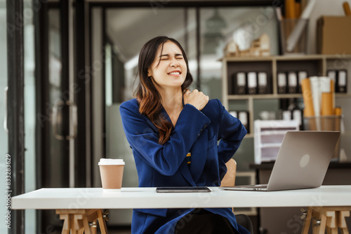 Young woman and other Asian individuals in formal suits work at desks with laptops, addressing concerns such as office syndrome, ergonomics, musculoskeletal disorders, and computer vision syndrome.