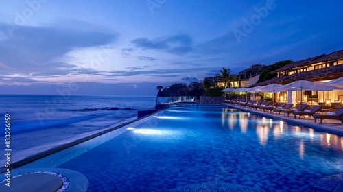Luxurious Beachfront Resort At Sunset With Illuminated Infinity Pool In Tropical Paradise