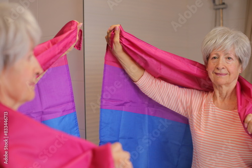 Proud senior woman waving the bisexual flag in front of the mirror 