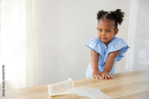 little African girl spilling milk and feeling sad on the table