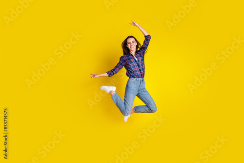 Full length photo of lovely young lady jump have fun dressed stylish plaid garment isolated on yellow color background