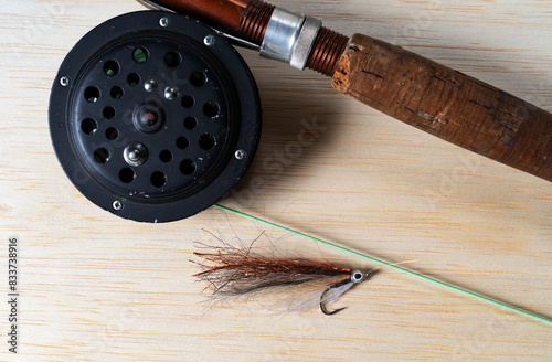 Close view of an old flyfishing rod and reel with a streamer fly on a wood tabletop.