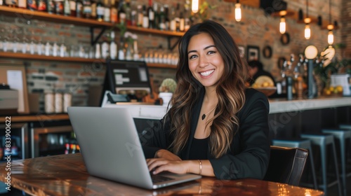 Happy young Latina businesswoman in suit working with laptop in a cafe or bar smiling confidently, for business owner, self employment, work from home, manager, small business, remote working concept.