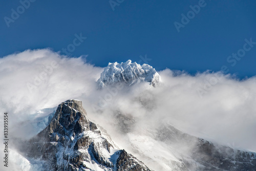 Close up view of snow covered summit Cerro Paine Grande of Cordillera Paine mountain group in Paine Massif, Torres del Paine National Park, Patagonia, Chile surrounded by white clouds