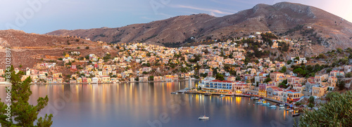 Panoramic view of Symi Island harbor with colorful houses and boats at dusk, Greece