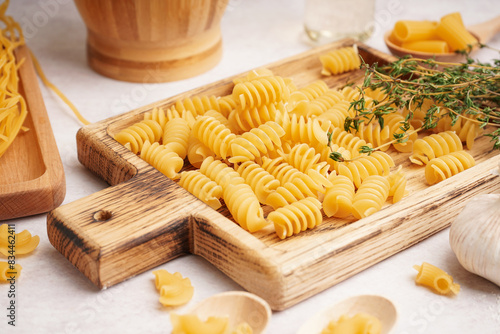 Wooden board with uncooked fusilli pasta and thyme on light background, closeup