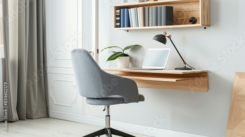 A minimalist office nook with a floating desk, a compact chair, and a laptop. The desk is clean, with a small plant and a notebook. The background shows a bright room with white walls and a modern