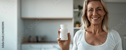 happy middle-aged woman is holding up a white supplement bottle. Pills, pharmaceuticals and drugs mockup concept.