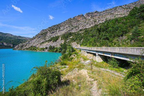 Road bridge parallel to the shore of the Lake of Castillon in the southern Alps in France - This reservoir with turquoise waters submerged the former village of Castillon in 1948