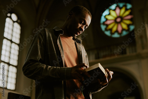 Low angle view medium shot of African American man standing in Catholic church reading religious text in book