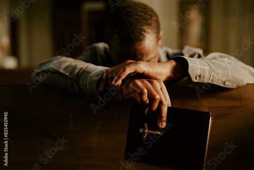Medium closeup of unrecognizable Black man sitting in Catholic church with Bible in hand praying to God