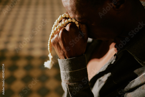 Closeup of unrecognizable African American man holding rosary spending time in church praying to God